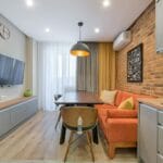 Małe mieszkanie z ceglaną ścianą, pomarańczową sofą i drewnianymi meblami