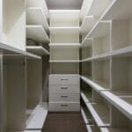 Wysoka szafa z pustymi półkami i metalowymi uchwytami w wąskiej garderobie