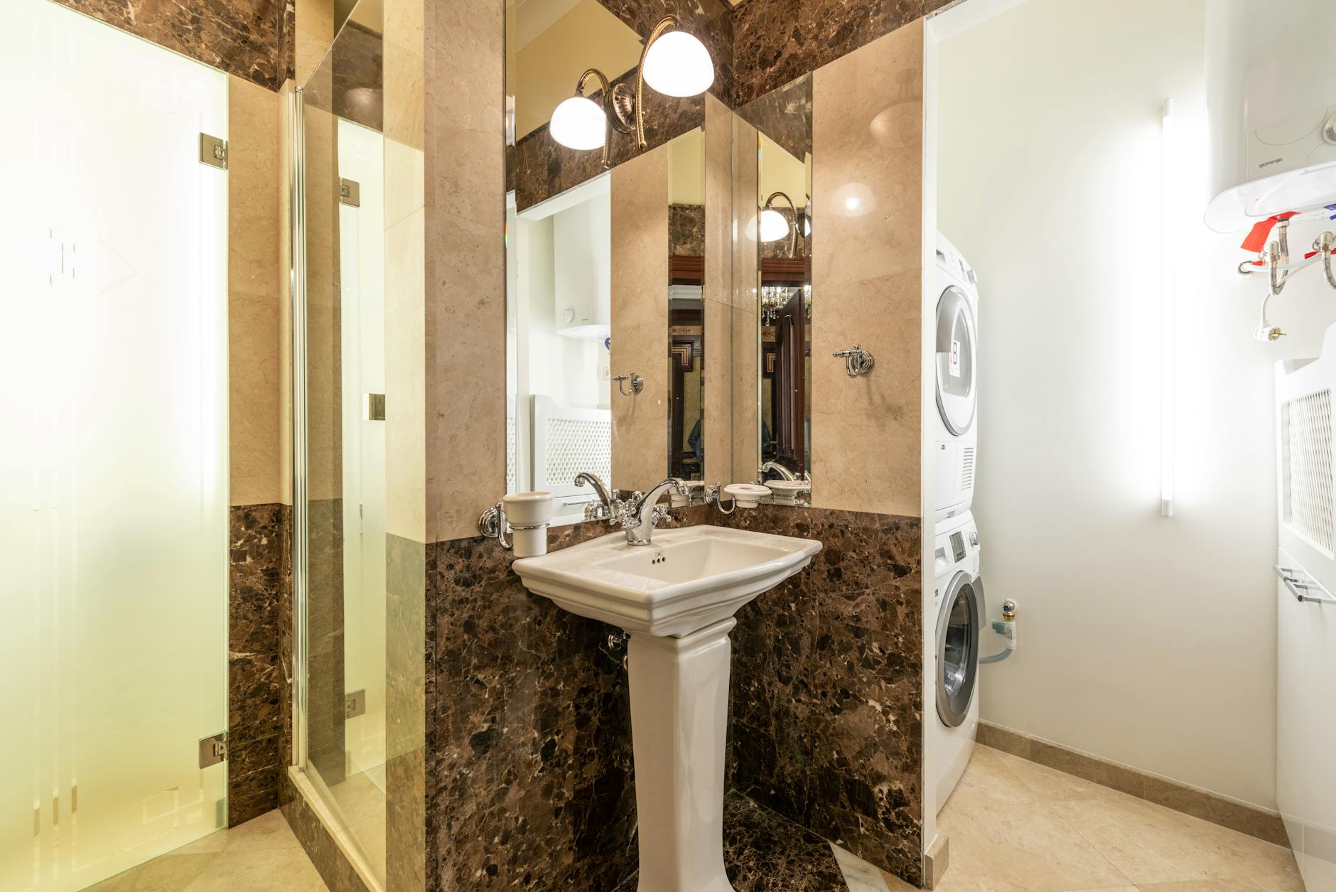 Łazienka z marmurowymi ścianami, umywalką na postumencie i pralko-suszarką