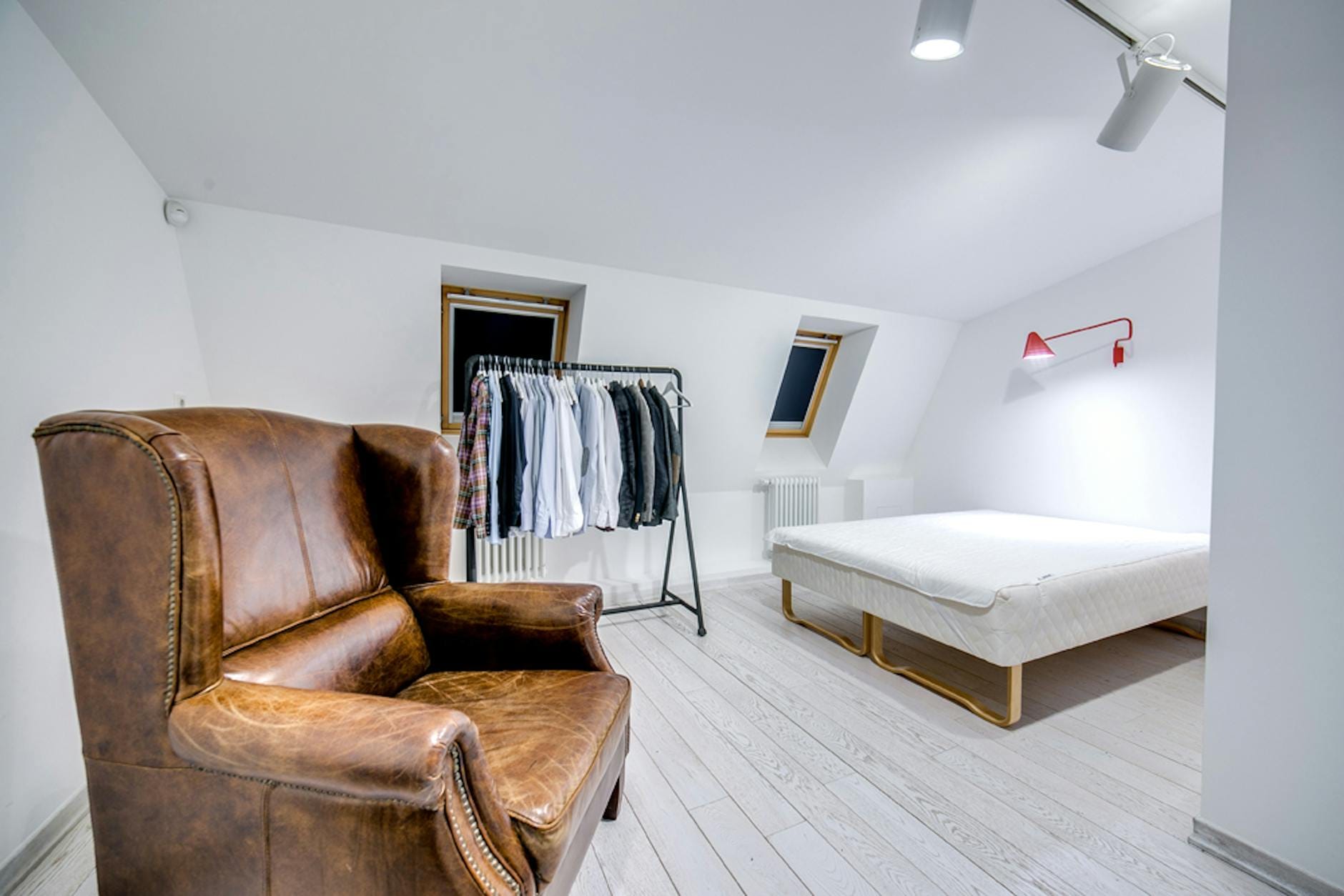 Minimalistyczna sypialnia z brązowym fotelem i otwartą garderobą