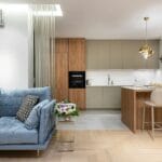 Jasny salon z kanapą i zabudową kuchenną pod sufit w małym mieszkaniu