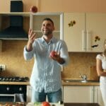 Para żongluje jabłkami w jasnej, nowoczesnej kuchni na wymiar