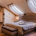 Jak urządzić sypialnię z nietypowym skosem? Pomysły na meble na wymiar Elegancka sypialnia z luksusową pościelą, drewnem i zasłonami